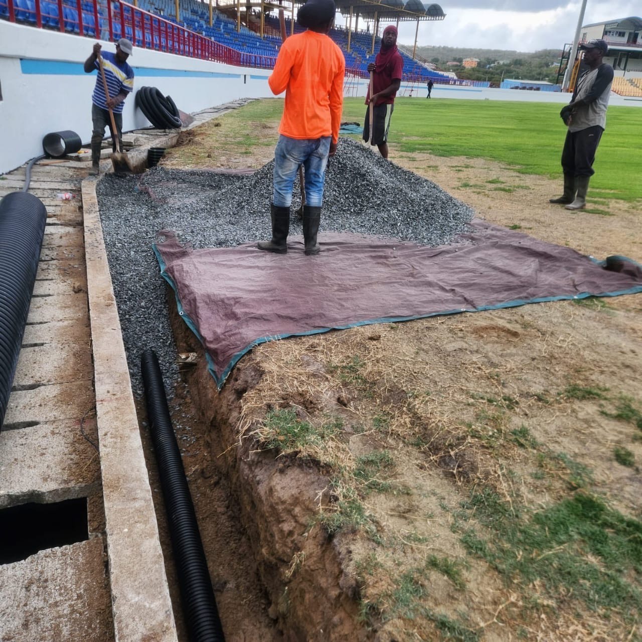 Drainage construction at Darren Sammy Cricket Grounds in Saint Lucia with piping reinforced by stone backfill for water management.